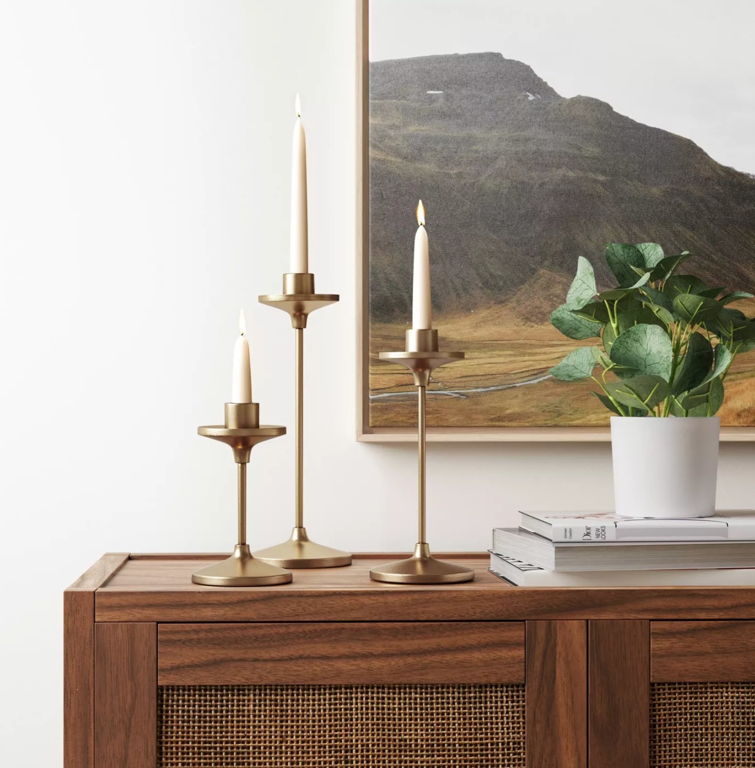 the three candle holders with candles in them next to a wall painting and a plant