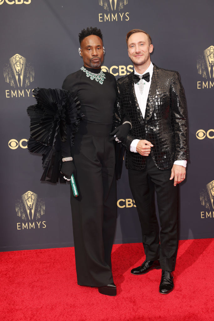 Billy Porter wears a dark jumpsuit with puffy, ruffle sleeves and Adam Smith wears a dark suit