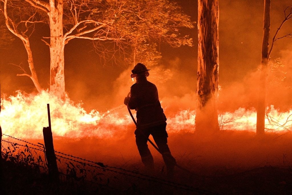 A firefighter hosing down trees and flying embers in an effort to secure nearby houses from bushfires near the town of Nowra in the Australian state of New South Wales