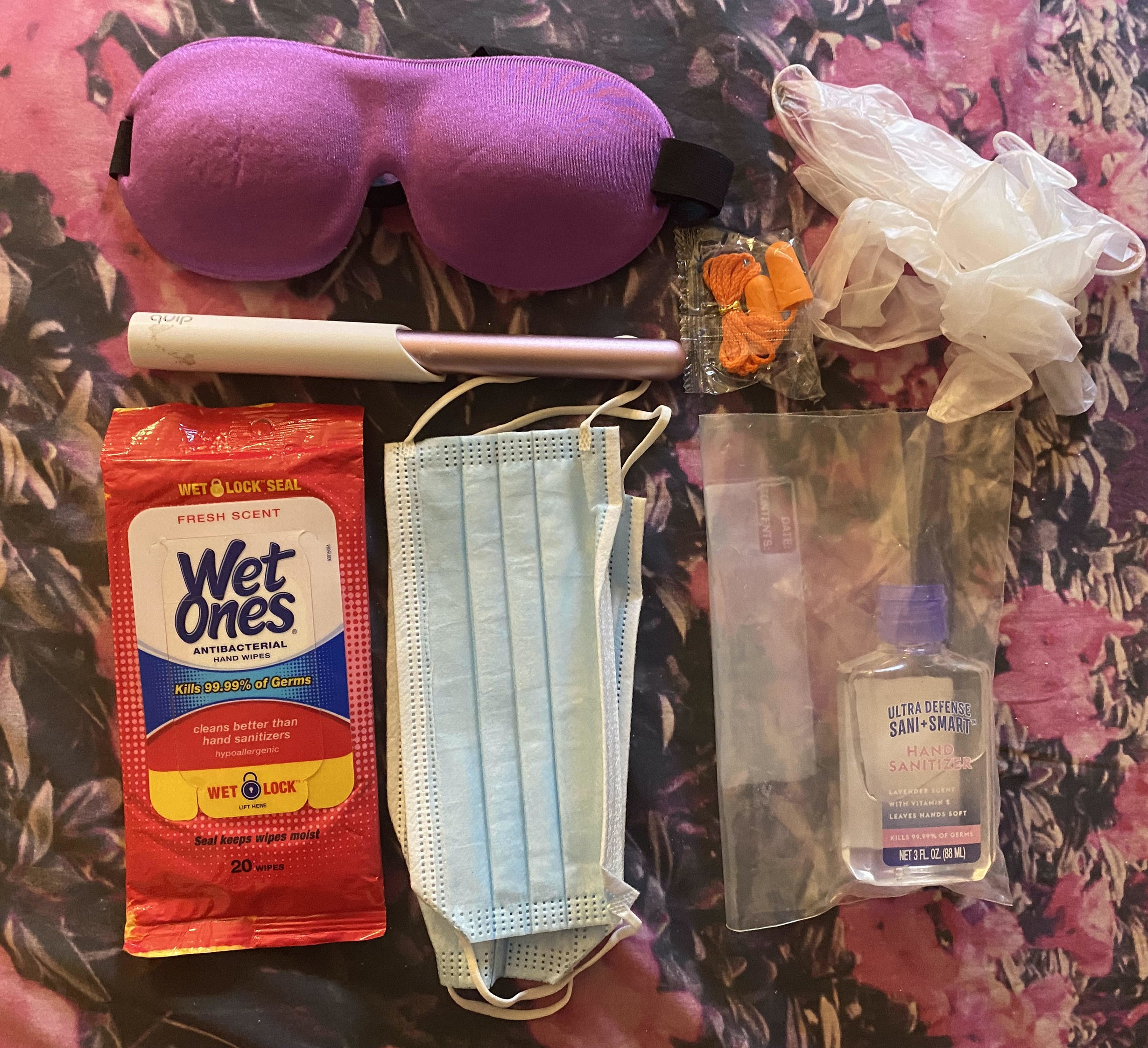 various plane carry on essentials like hand sanitizing wipes, masks, a bottle of hand sanitizer in a separate bag.