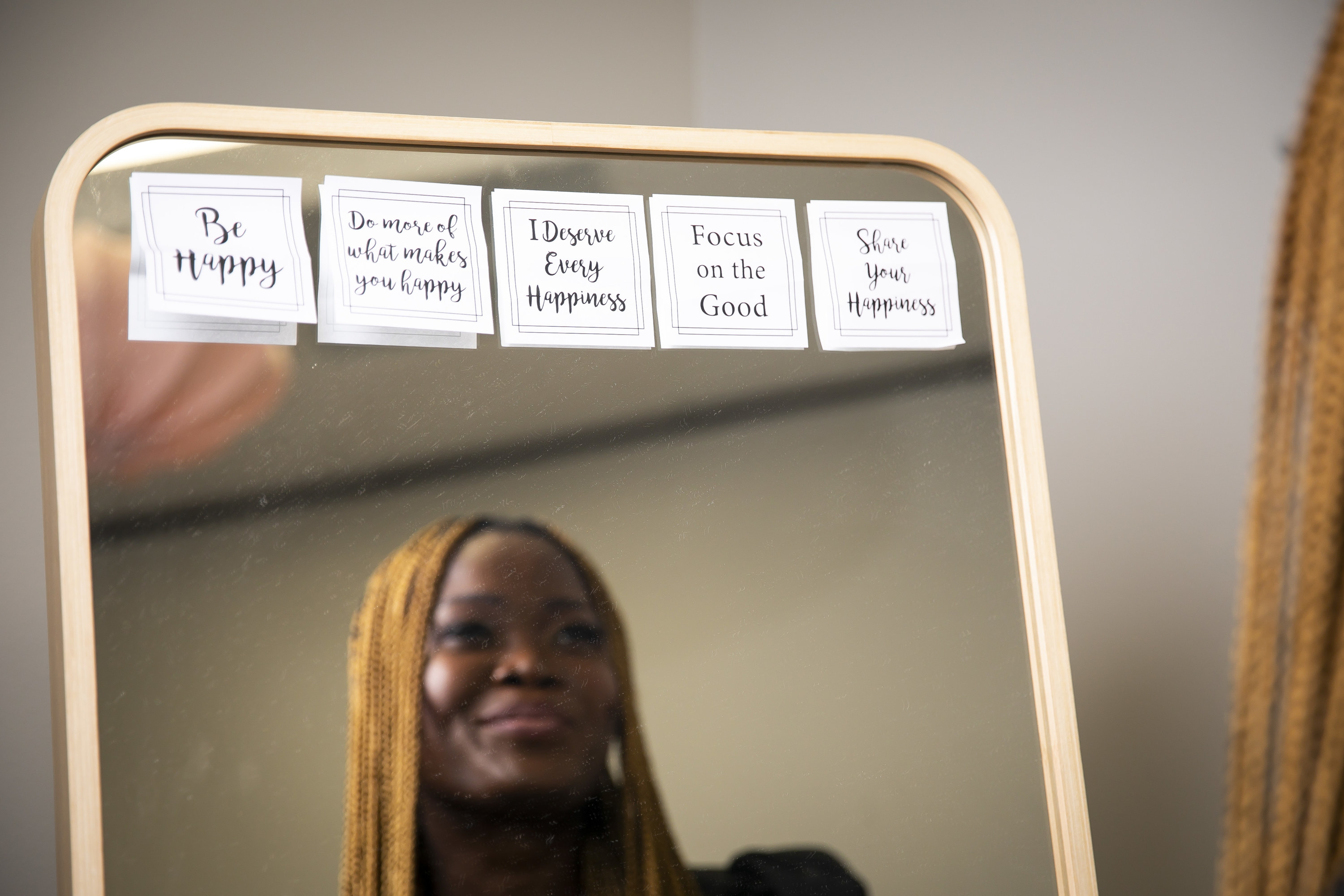 A woman looking in a mirror with inspirational messages like &quot;be happy,&quot; &quot;share happiness,&quot; &quot;focus on the good&quot;