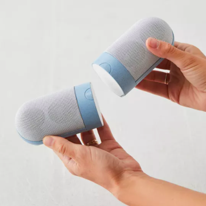 Someone holding up the two bluetooth speakers; they attach magnetically to each other
