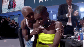 GIF of Michaela standing up from her table at the Emmys, with Cynthia Erivo talking to her