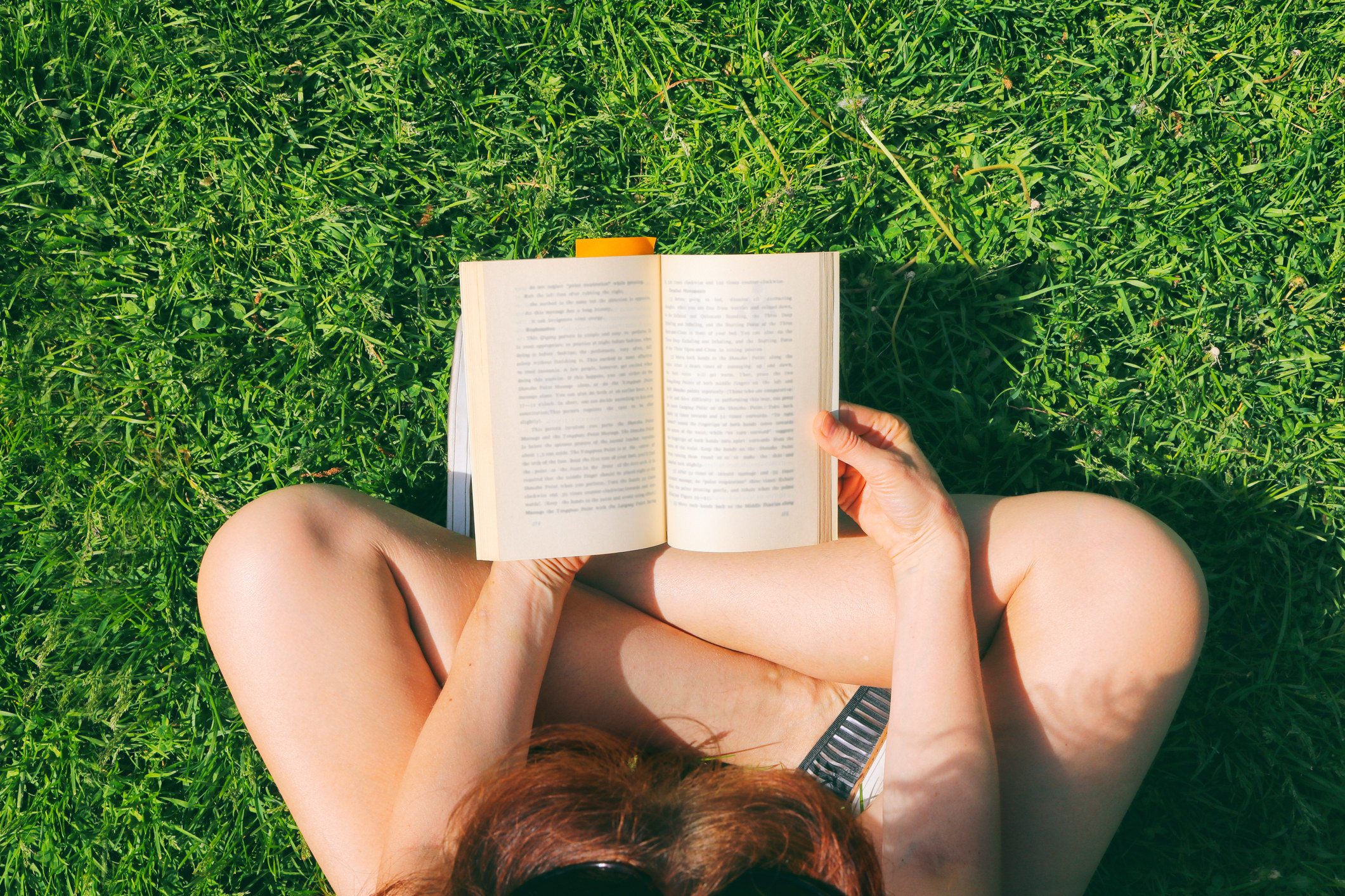 Young woman sitting on the grass in park and reading the book