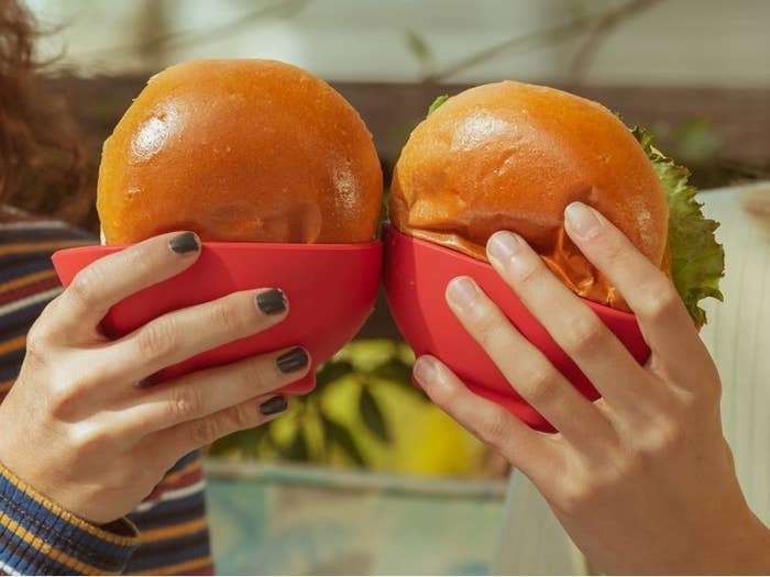 two people holding hamburgers that are placed in the silicone holders
