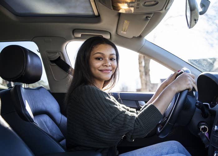 A woman smiling as she sits in the driver&#x27;s seat of a car with her seatbelt on