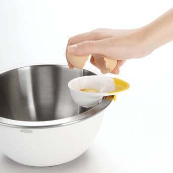 hand cracking an egg on the yellow and white egg-shaped separator attached to the rim of a bowl