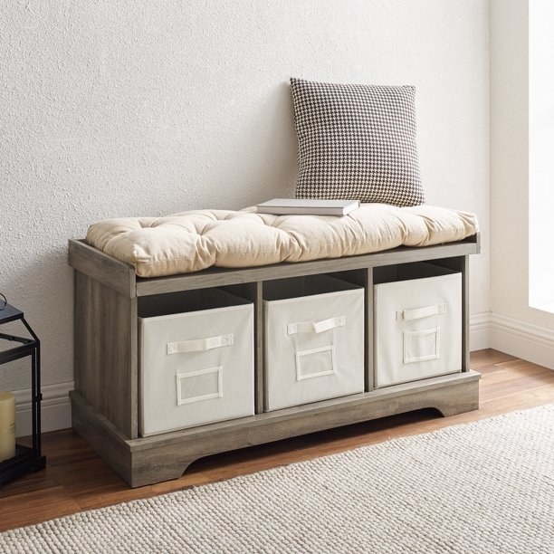 Storage bench with three baskets, tufted cushion and pillow with a book sitting on top.
