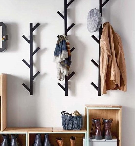 Three black metal coat racks hung on the wall above a bench, with a coat, hat and scarf hanging on them.