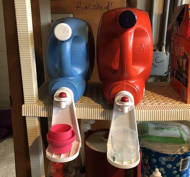 a reviewer photo of two bulk detergent bottles with the cup holders attached to the spouts