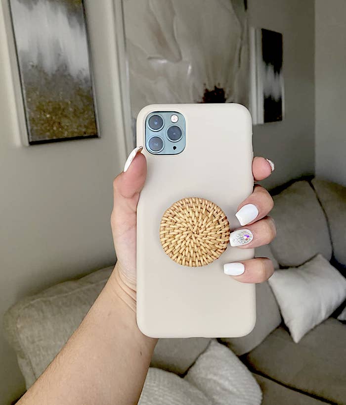 reviewer holding phone with the rattan phone grip attached to the back
