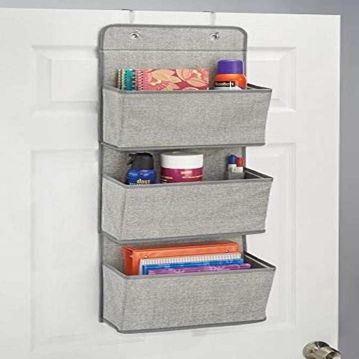 Cascading organizer hanging on door, holding office supplies.