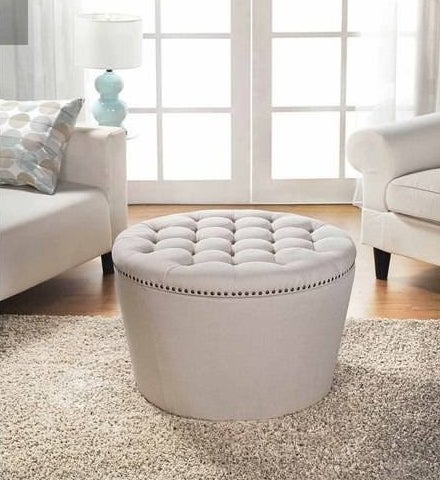 Tufted storage ottoman in &quot;cream&quot; color shown in a living room next to an armchair and sofa, on top of a textured rug.