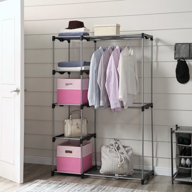 Shelf shown holding shirts on hangers, two large pink storage baskets, bags and other items.