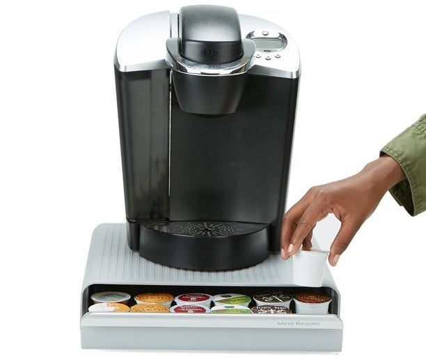 Hand reaching into open drawer holding coffee pods.