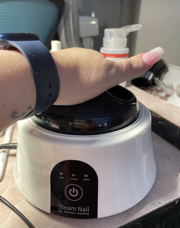 Reviewer with their hand in a small white steam nail machine with three settings