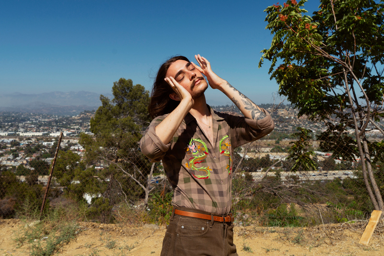 Gaca standing with his eyes closed and pushing his hair back, overlooking Hollywood