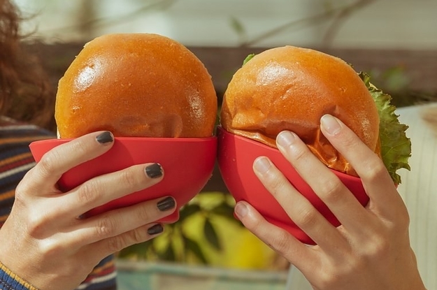 two people holding hamburgers that are placed in the silicone holders