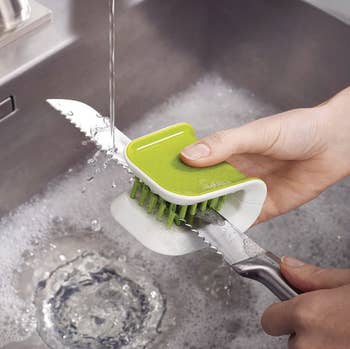 A model washing a knife with a green, non-slip knife brush 