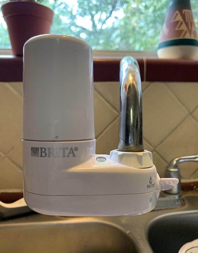 A reviewers white, tap water filtration system over the kitchen sink faucet