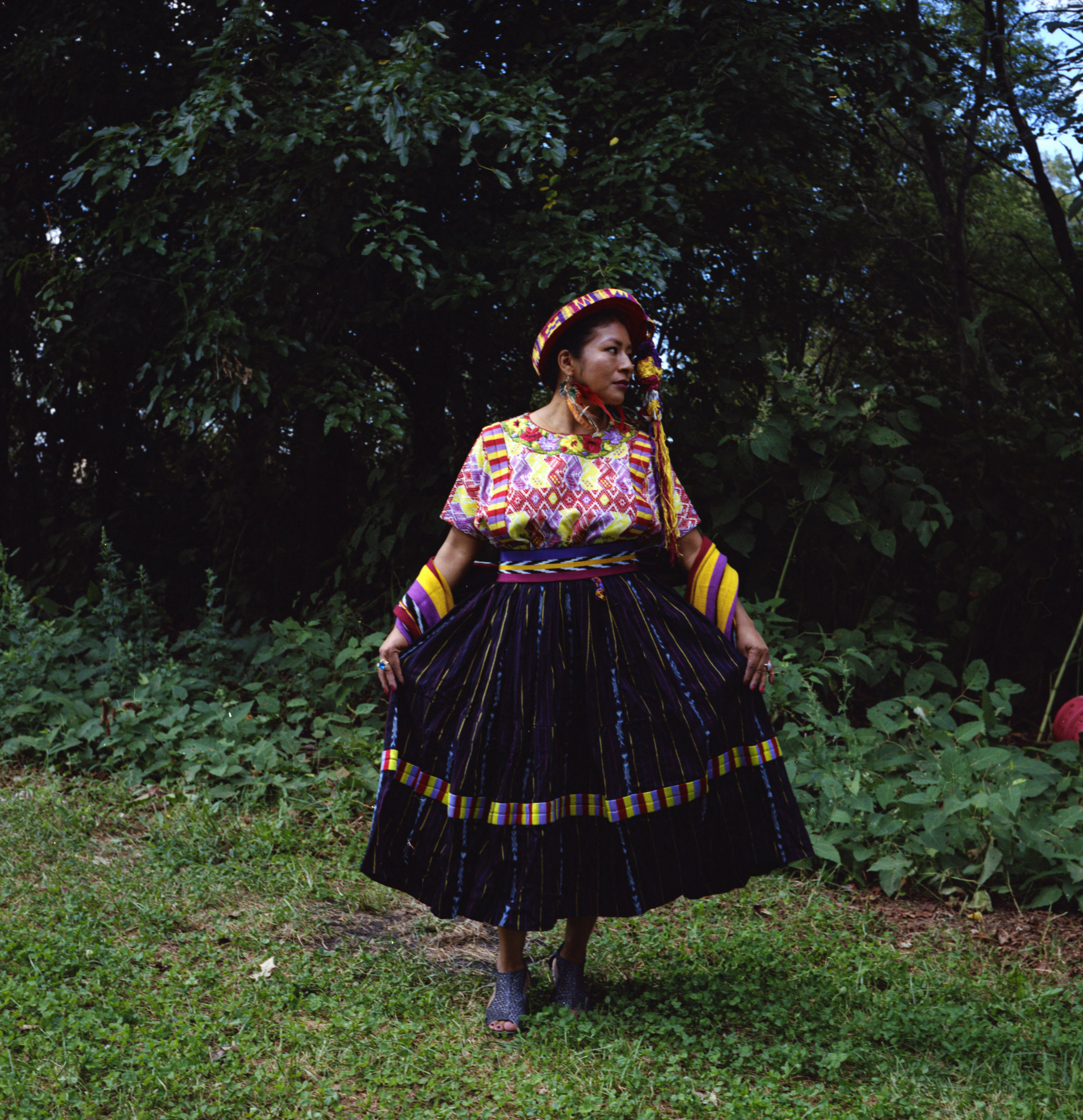 A woman in a black skirt and colored shirt in a garden, facing away from the camera