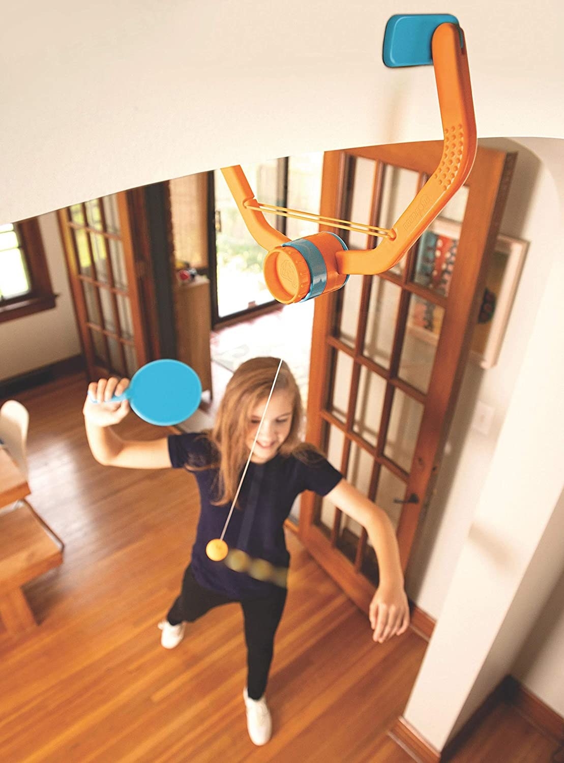 Child model playing ping pong with toy hanging from doorway