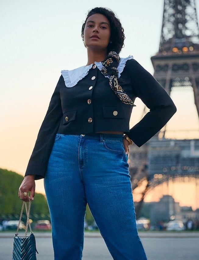 model standing in front of Eiffel Tower in black cropped jacket with white ruffle collar and gold buttons