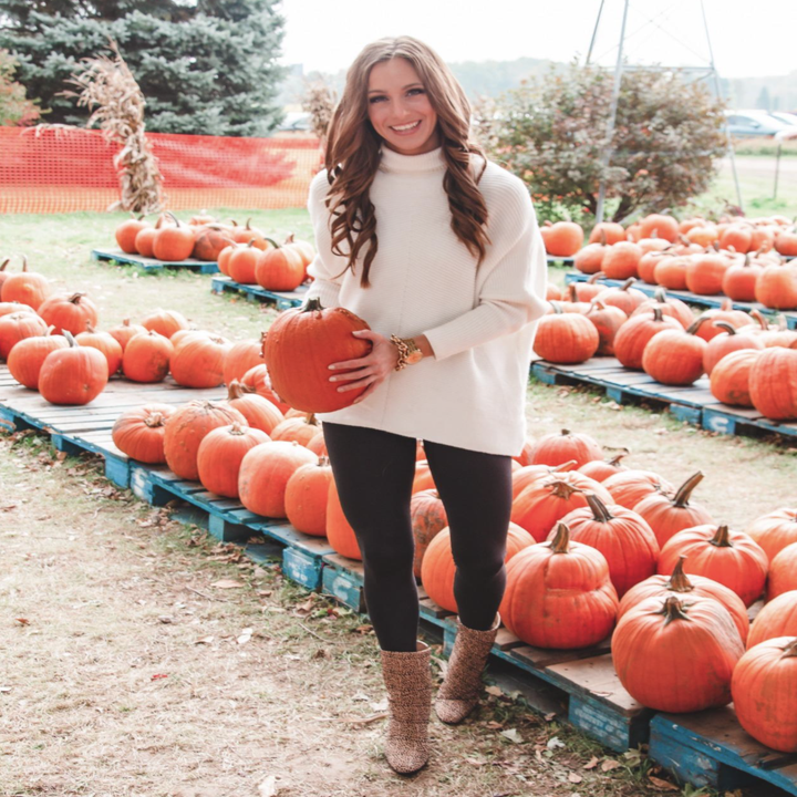 Reviewer wearing oversized cream colored sweater in a pumpkin patch