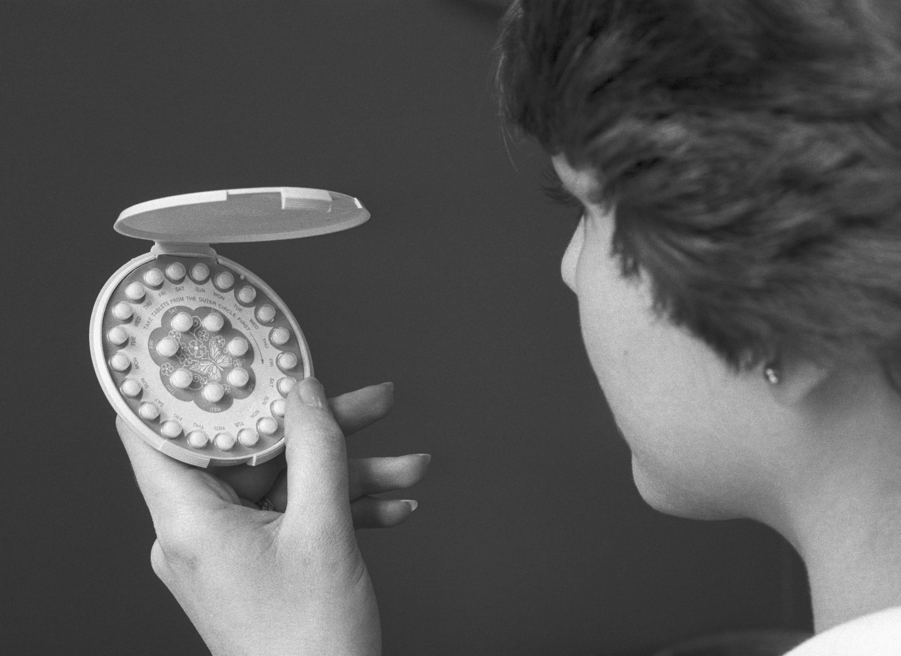 A black and white photo of a woman staring at an old pack of birth control