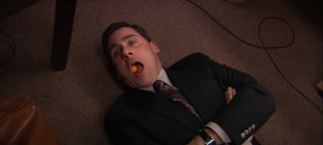 A man lying down on the floor with a cheeseball in his mouth