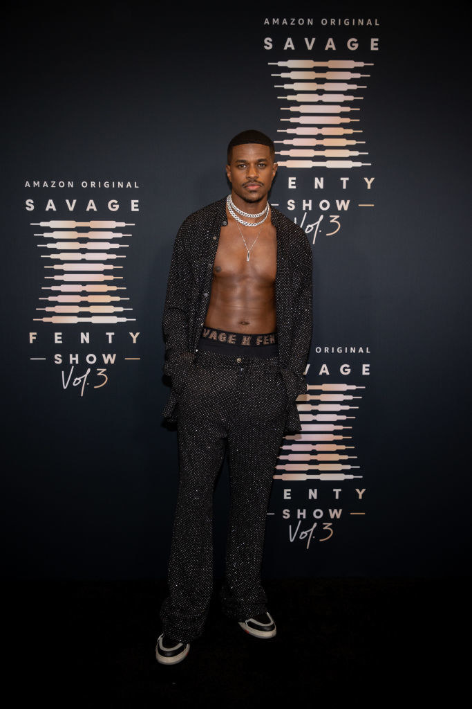 Jeremy is posing on the red carpet in a glittery open shirt and matching pants and boxers with the top showing the Savage X Fenty logo