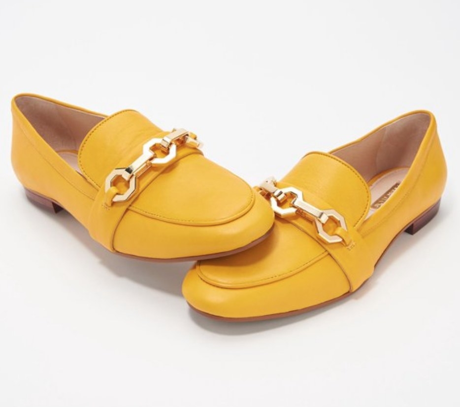 A pair of yellow, slip-on loafers with a gold chain
