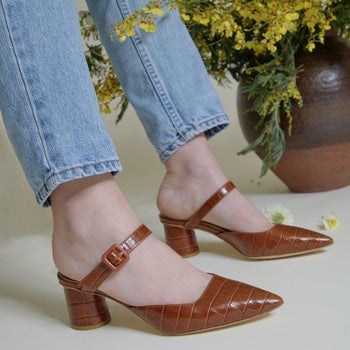 a model wearing jeans and the mules in brown crocodile embossed leather 