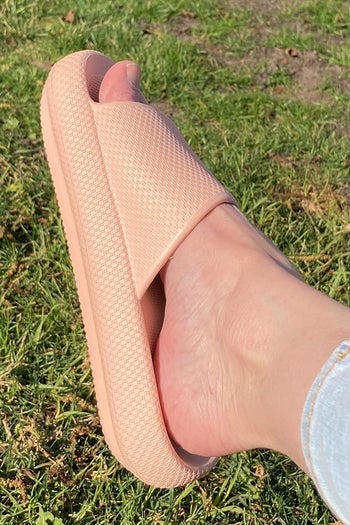 a profile view of a reviewer wearing the slippers in light pink outside