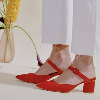 a model wearing white pants and the mules in red suede 
