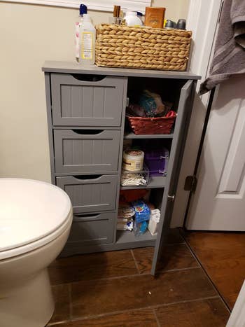 Reviewer photo of the grey organizer in their bathroom but the cabinet door is open, revealing three shelves inside