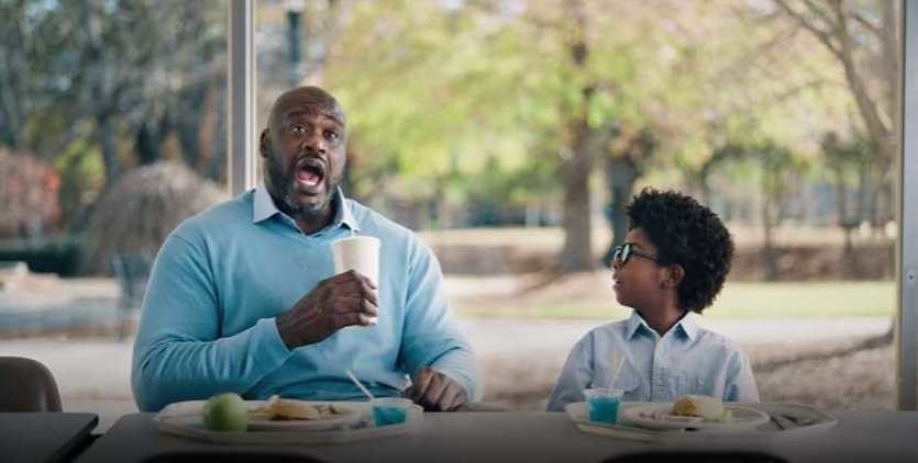 Shaq sips drink next to little kid at a lunch table