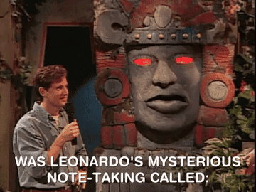 TV show host stands before Talking Olmec head as he asks &quot;Was Leonardo&#x27;s mysterious note-taking called: Morse Code, Mirror Writing or—&quot;