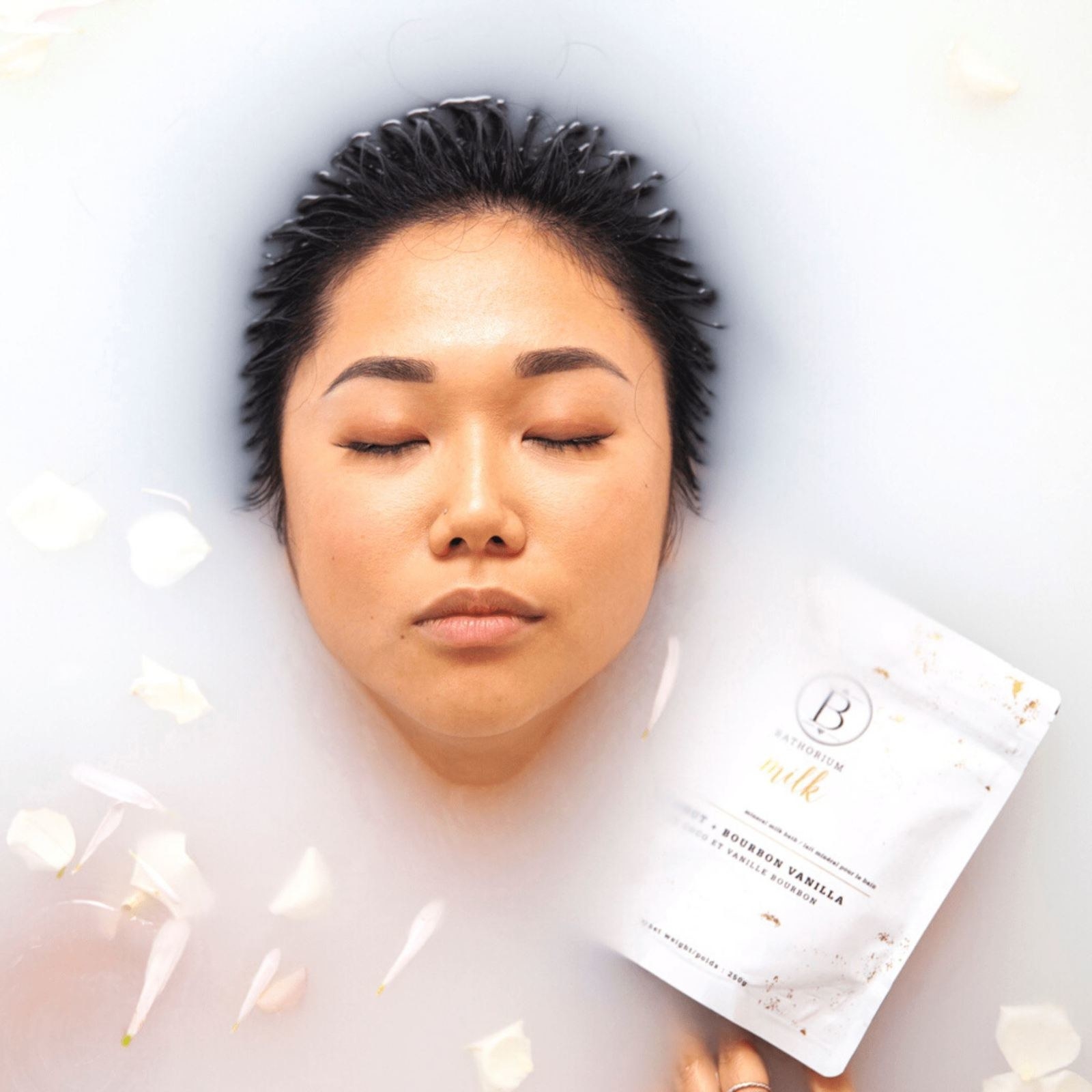 model inside a milky bath with the product packaging by their face