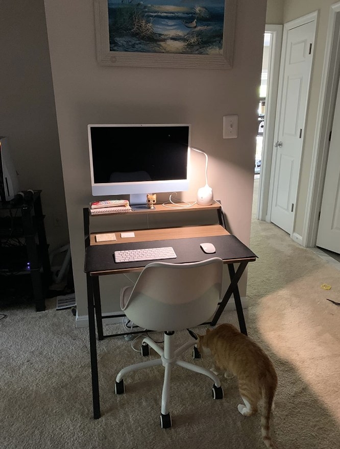 Foldable desk with computer monitor on it, keyboard and desk lamp, white chair in front