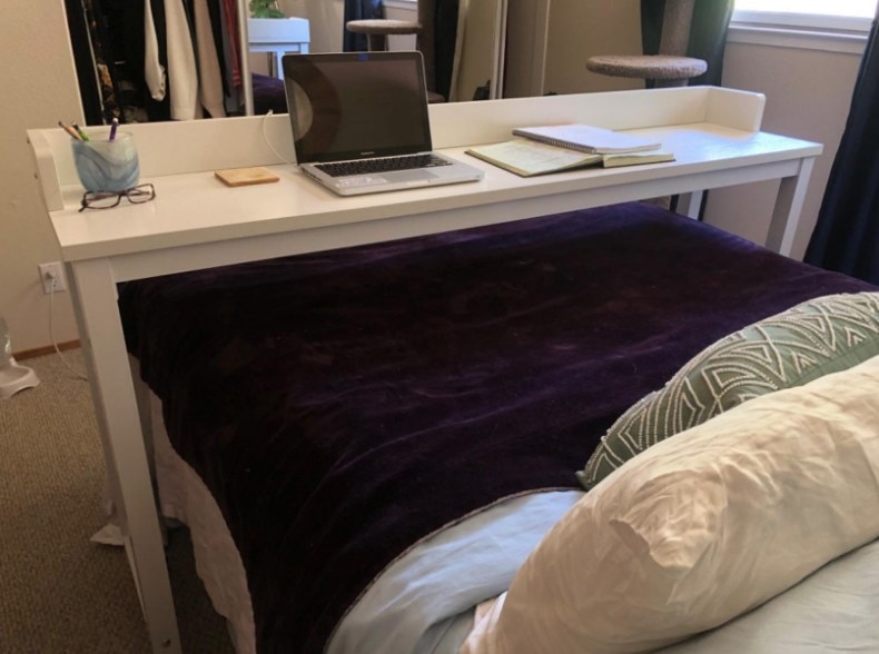 White table with laptop and notebooks on it over bed