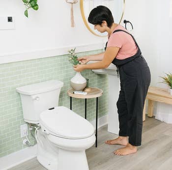 the toilet seat attached to a tank inside a stylized bathroom with a person standing beside it