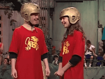 Two contestants (boy and girl) on Legends of The Hidden Temple stand together. The girl is embarrassed and laughs