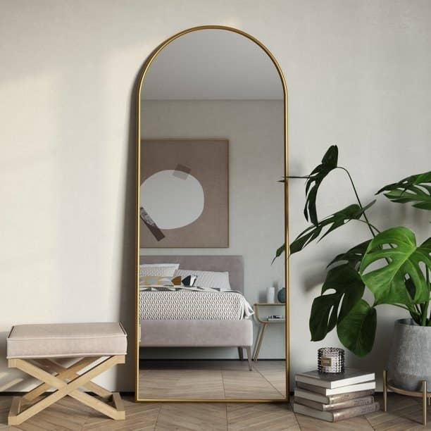 The arched mirror with a gold frame leaning against a bedroom wall