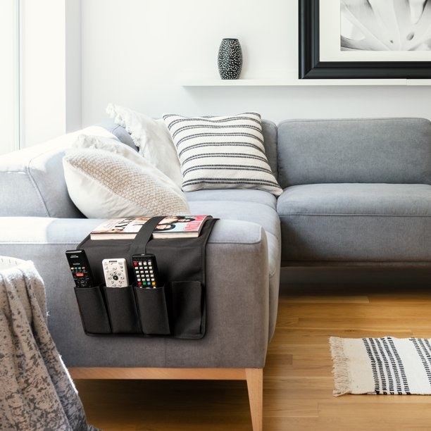 A grey couch with black remote caddy on the arm