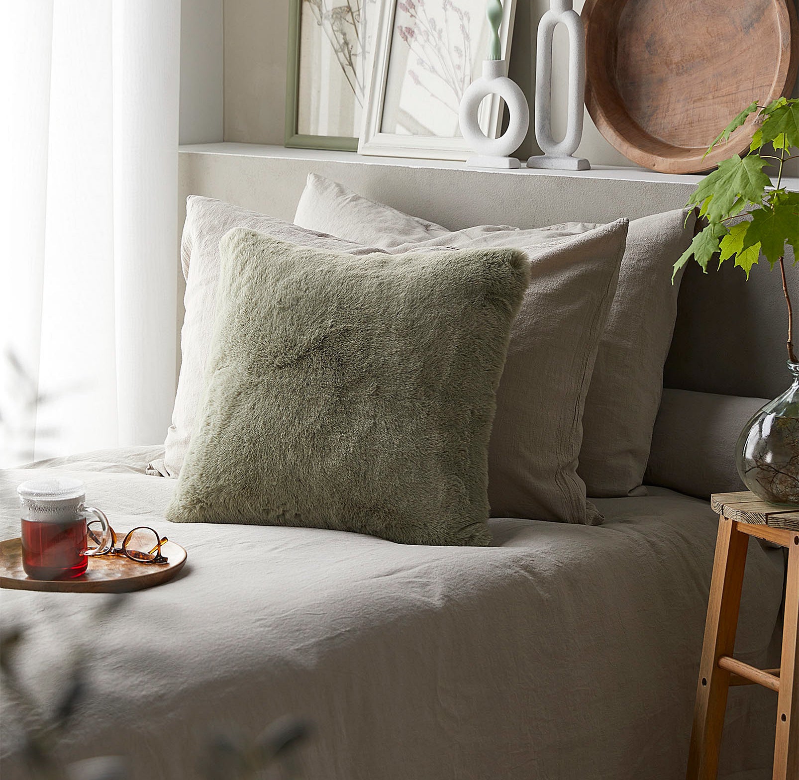 A fluffy throw pillow on a bed with a blanket