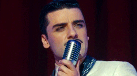 GIF of Oscar Isaac singing into an old microphone and winking