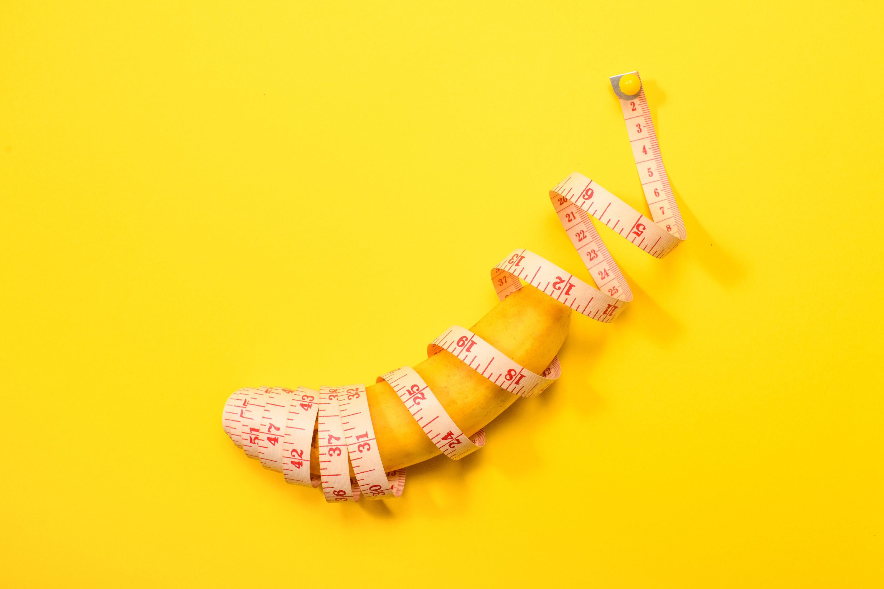 A banana wrapped in measuring tape on a yellow background