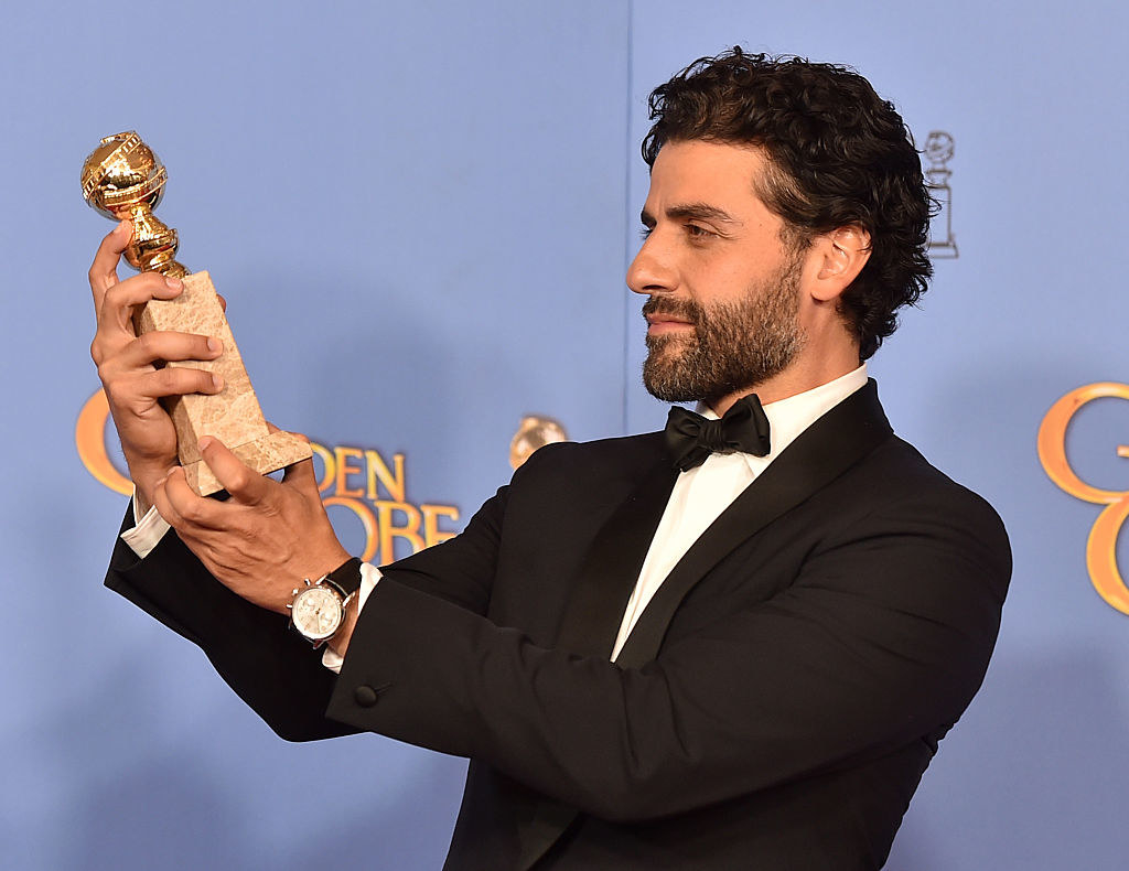Oscar Isaac holding his Golden Globe award up so he can look right at it