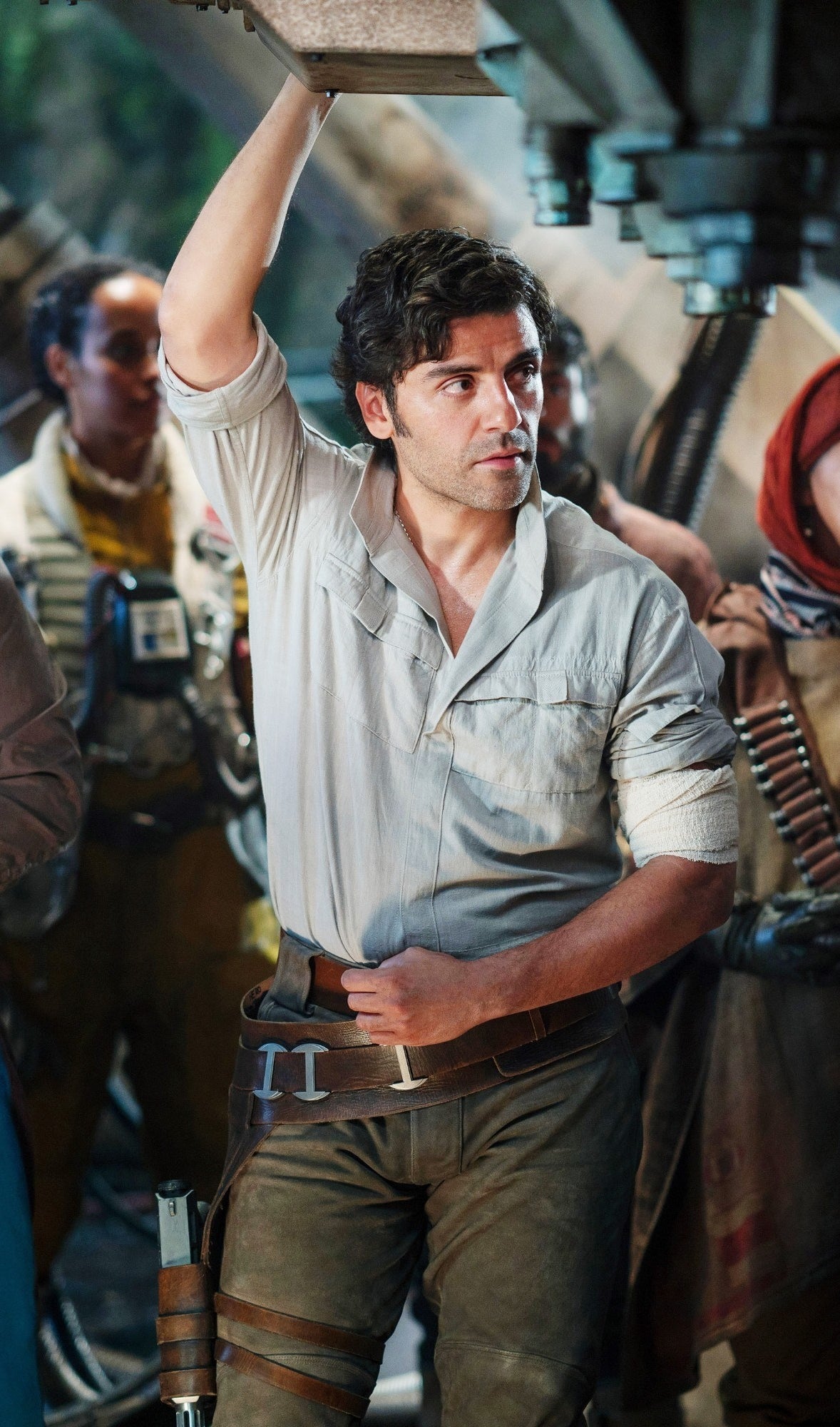 Oscar Isaac dressed as Poe Dameron on Star Wars set, arm up and leaning
